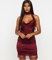Woman wearing a burgundy halter neck dress with fringe details on a white background