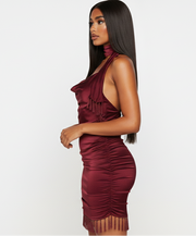 Woman wearing a burgundy halter neck dress with fringe details on a white background