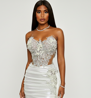 Woman wearing a strapless, embellished white dress on a plain background