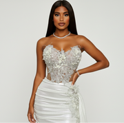 Woman wearing a strapless silver and white evening gown on a plain background