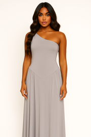 Woman wearing a one-shoulder gray dress against a white background