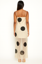 Woman wearing a beige slip dress with black polka dots on a white background